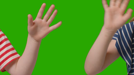 Close-Up-Of-Two-Young-Children-Waving-To-Camera-Against-Green-Screen-1